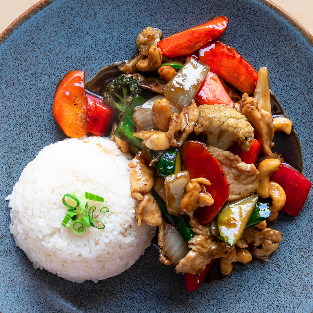 Poulet servi avec poivrons, oignons, carottes et champignons aromatisés à l'huile de noix de cajou, garni de noix de cajou rôties glacées.